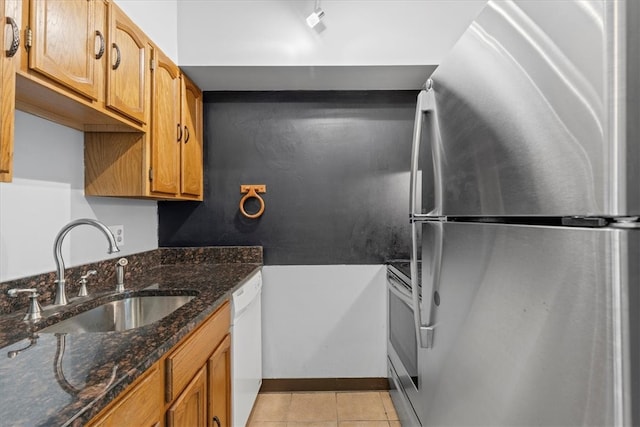 kitchen featuring dark stone counters, stainless steel appliances, light tile flooring, and sink