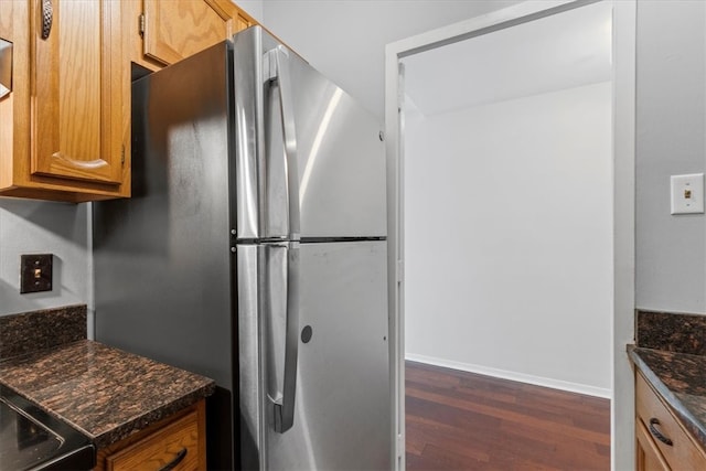 kitchen with dark stone countertops, stainless steel fridge, and dark wood-type flooring