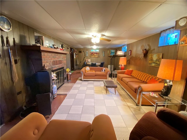 living room featuring a drop ceiling, wood walls, a fireplace, and ceiling fan