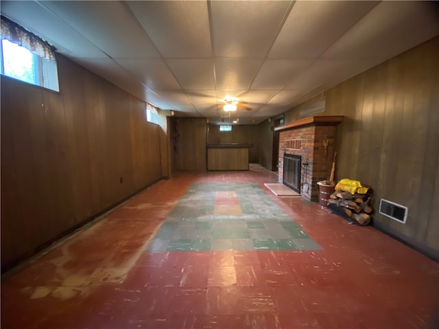 basement featuring a healthy amount of sunlight, wooden walls, and a brick fireplace