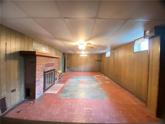 basement featuring wood walls, a drop ceiling, and a brick fireplace