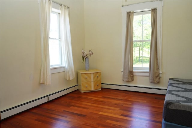 bedroom featuring dark hardwood / wood-style flooring, multiple windows, and a baseboard heating unit