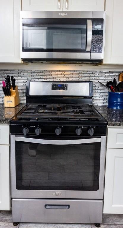 interior space with white cabinetry, stainless steel appliances, and dark stone countertops