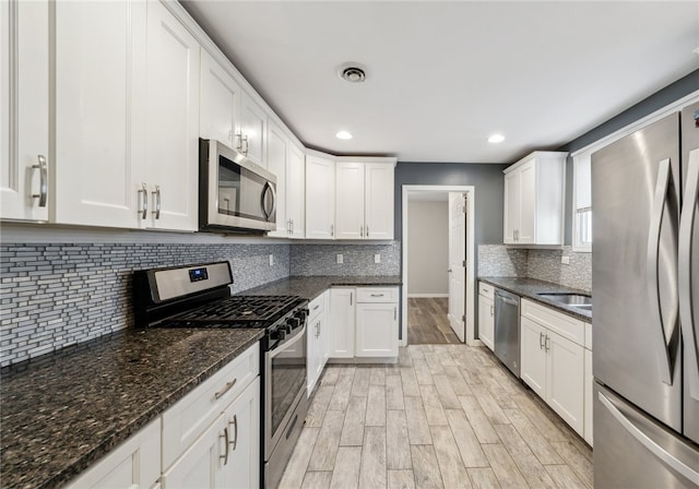 kitchen featuring white cabinetry, stainless steel appliances, and dark stone counters