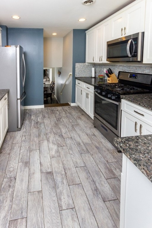 kitchen with decorative backsplash, stainless steel appliances, dark stone counters, and white cabinets