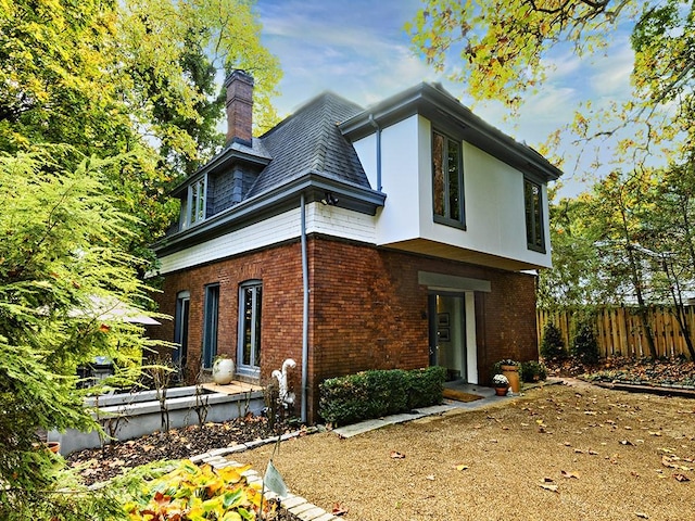 view of front of house with a chimney, fence, and brick siding