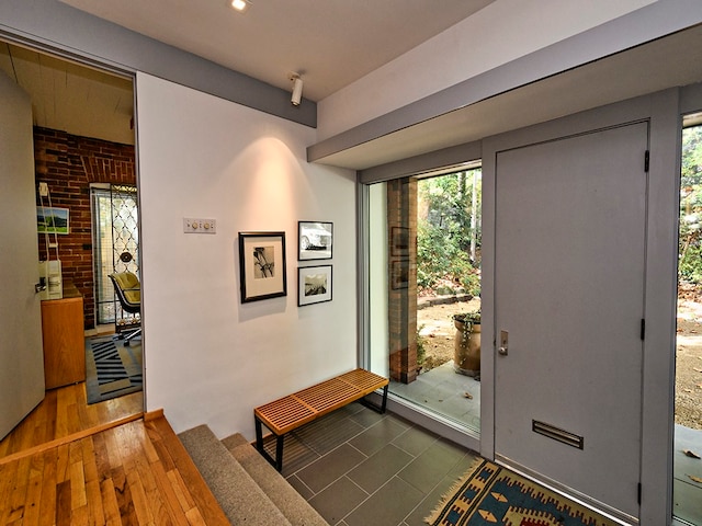 entrance foyer featuring brick wall and dark wood-type flooring