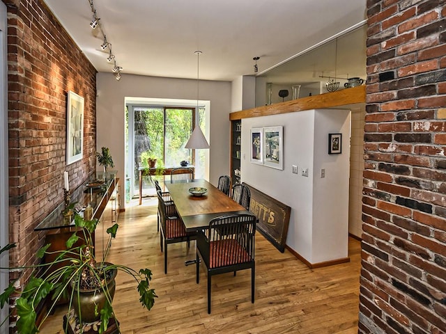 dining space featuring rail lighting, baseboards, brick wall, and light wood finished floors