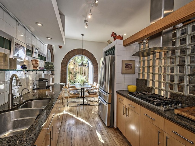 kitchen featuring stainless steel appliances, dark stone countertops, a sink, light wood-style floors, and backsplash