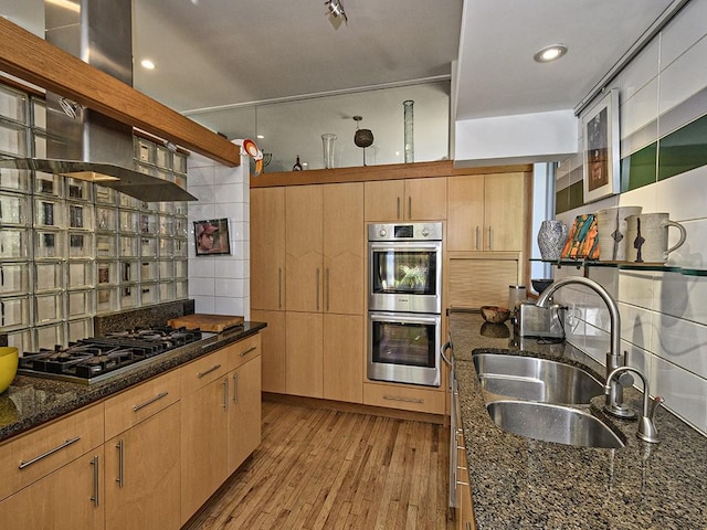kitchen with decorative backsplash, light wood-style flooring, dark stone counters, appliances with stainless steel finishes, and a sink