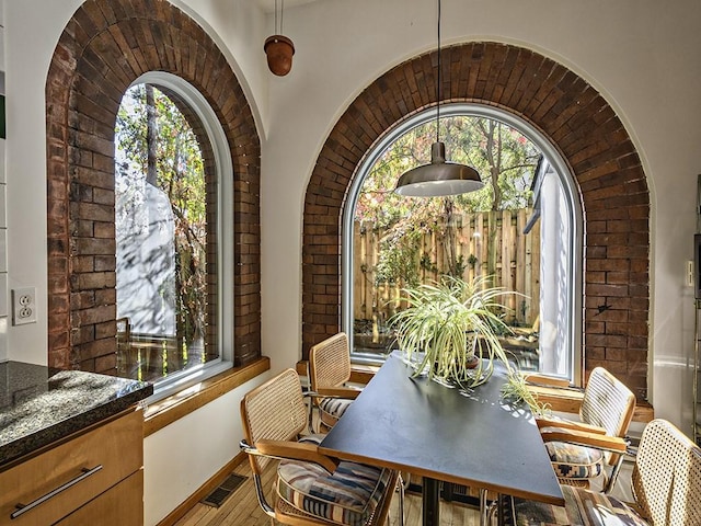 dining room featuring baseboards, arched walkways, brick wall, visible vents, and wood finished floors