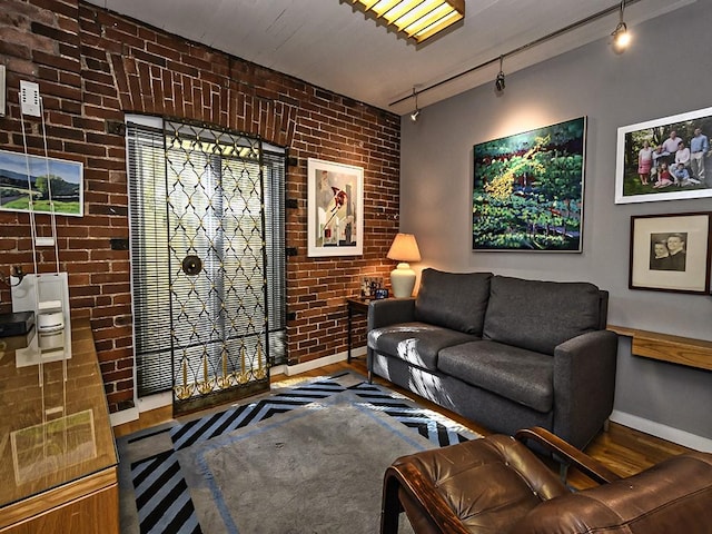 living area featuring rail lighting, baseboards, brick wall, and wood finished floors