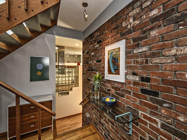 hall with baseboards, brick wall, stairway, and wood finished floors
