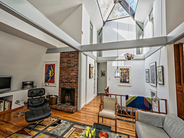 living room featuring light hardwood / wood-style flooring, a brick fireplace, brick wall, a towering ceiling, and a skylight