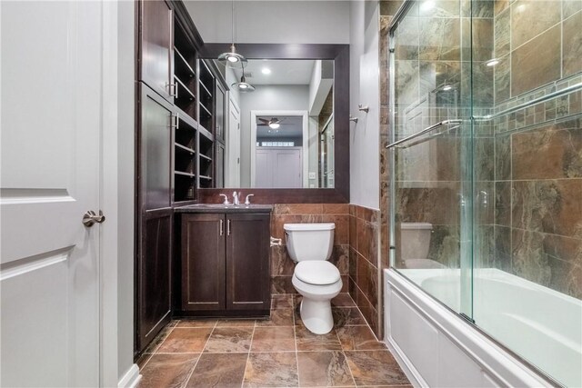 full bathroom featuring tile walls, ceiling fan, toilet, tile flooring, and bath / shower combo with glass door