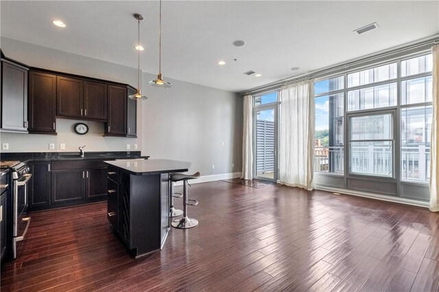 kitchen featuring hanging light fixtures, a kitchen island, dark hardwood / wood-style flooring, stainless steel range, and a kitchen bar