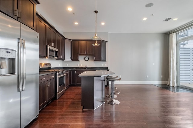 kitchen featuring dark hardwood / wood-style flooring, a center island, dark brown cabinets, appliances with stainless steel finishes, and pendant lighting