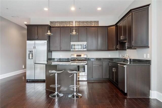 kitchen featuring a center island, dark hardwood / wood-style flooring, appliances with stainless steel finishes, decorative light fixtures, and a breakfast bar