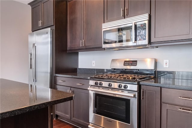 kitchen with dark stone counters, dark brown cabinets, dark wood-type flooring, and appliances with stainless steel finishes