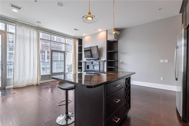 kitchen featuring a center island, a kitchen breakfast bar, hanging light fixtures, dark wood-type flooring, and stainless steel refrigerator