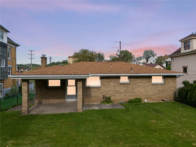 back house at dusk with a patio area and a lawn