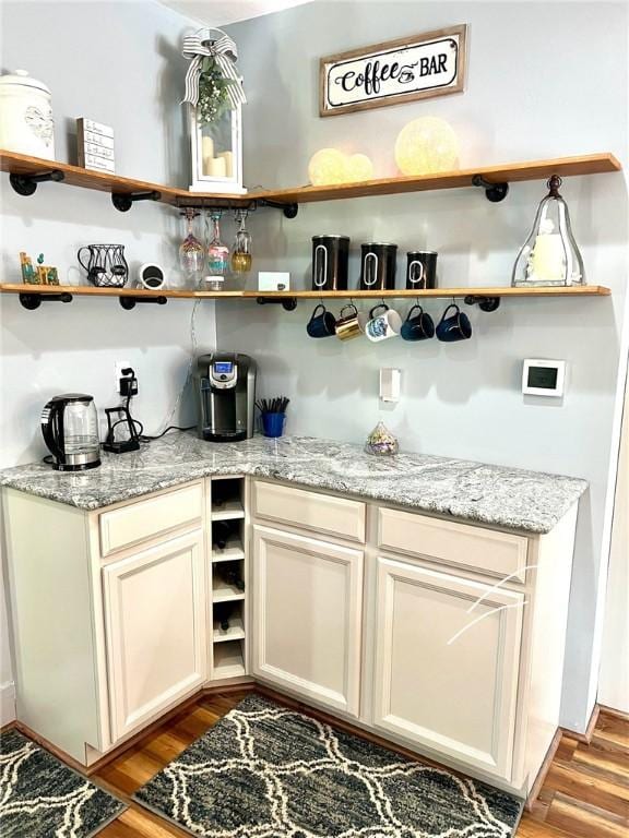 bar with light stone countertops, cream cabinets, and light wood-type flooring