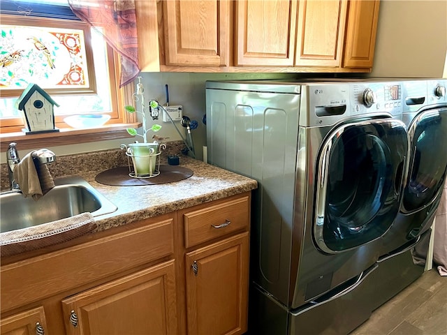 clothes washing area with cabinets, light wood-type flooring, washer and clothes dryer, and sink