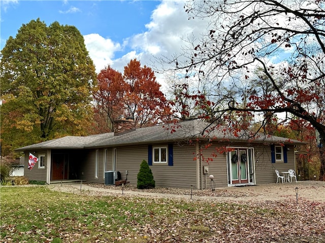 back of property featuring a chimney, a lawn, and central AC