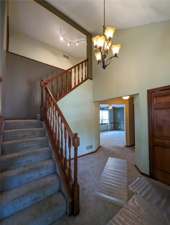 stairs with a towering ceiling, carpet floors, an inviting chandelier, and rail lighting