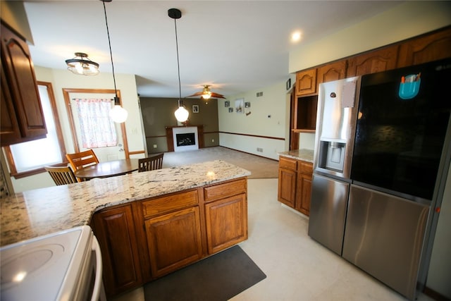 kitchen featuring hanging light fixtures, stove, ceiling fan, light stone countertops, and stainless steel fridge