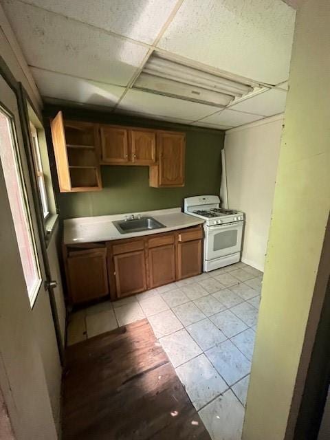 kitchen with white gas range, light tile patterned floors, a paneled ceiling, and sink