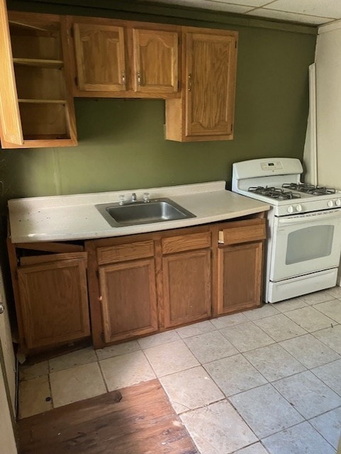 kitchen featuring sink, light tile patterned floors, a paneled ceiling, and white gas range oven