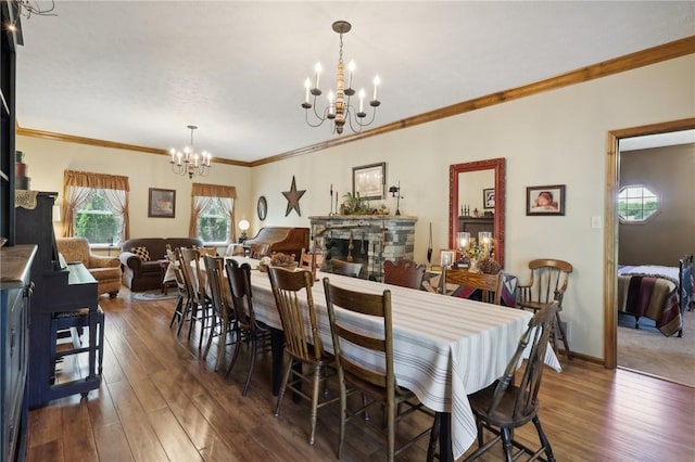 dining room featuring dark wood-type flooring, a stone fireplace, a notable chandelier, and crown molding