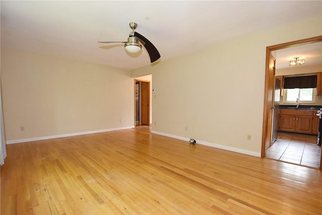 spare room featuring light wood finished floors, ceiling fan, baseboards, and a sink