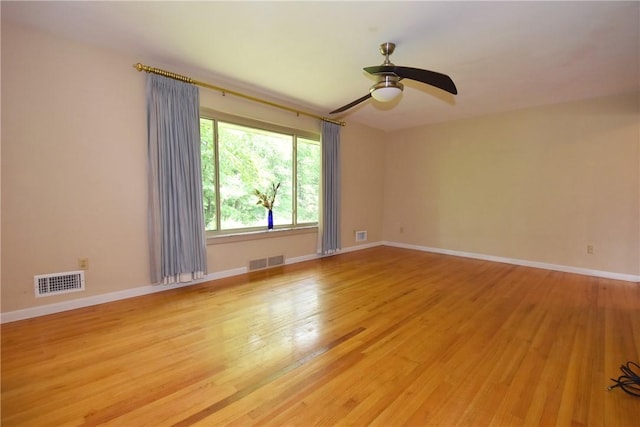 spare room featuring light wood-style flooring, a ceiling fan, visible vents, and baseboards