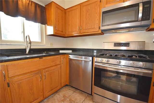 kitchen with appliances with stainless steel finishes, sink, dark stone countertops, and light tile flooring