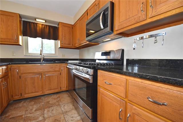 kitchen featuring appliances with stainless steel finishes, sink, light tile floors, and dark stone counters