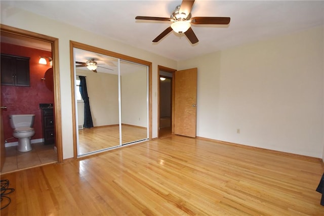 unfurnished bedroom featuring a closet, ensuite bathroom, light wood-style floors, ceiling fan, and baseboards