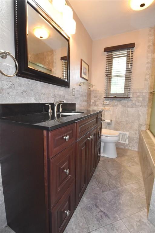 bathroom with toilet, vanity, visible vents, and tile walls