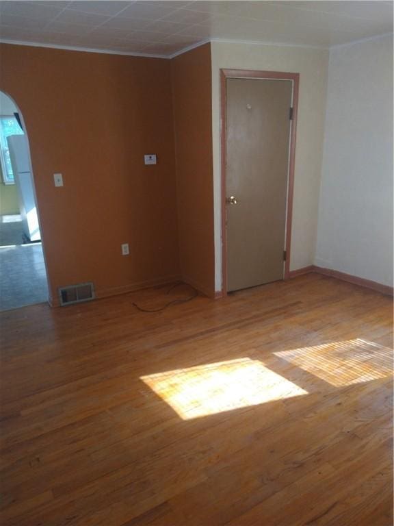 empty room with arched walkways, visible vents, baseboards, and wood finished floors