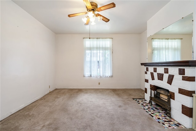 carpeted empty room featuring ceiling fan, a fireplace, and a wealth of natural light