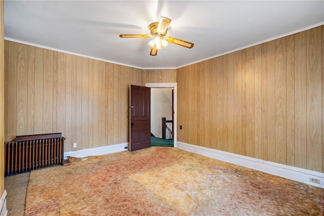 carpeted spare room with crown molding, wooden walls, ceiling fan, and radiator heating unit