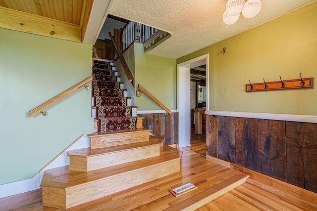 staircase featuring wooden walls, a textured ceiling, and hardwood / wood-style flooring