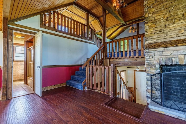 stairway with high vaulted ceiling, hardwood / wood-style flooring, a stone fireplace, and wooden ceiling