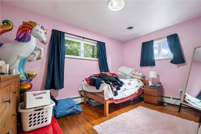 bedroom featuring hardwood / wood-style flooring and a baseboard heating unit