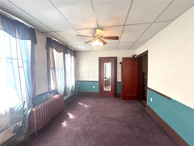 unfurnished room featuring dark colored carpet, a healthy amount of sunlight, a paneled ceiling, and ceiling fan