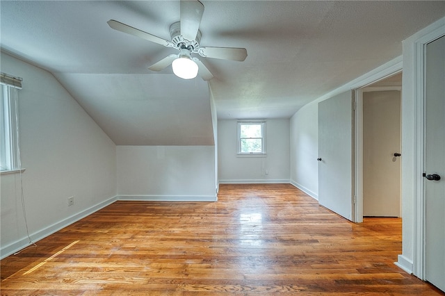 additional living space with lofted ceiling, a textured ceiling, light wood-type flooring, and ceiling fan