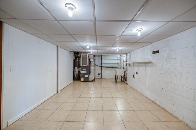 basement with sink, heating unit, light tile patterned floors, and a drop ceiling