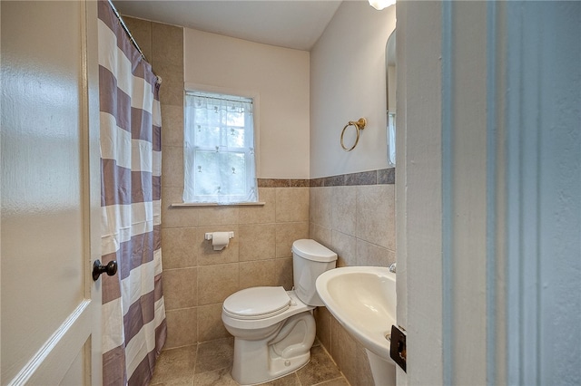 bathroom with toilet, sink, tile patterned floors, and tile walls