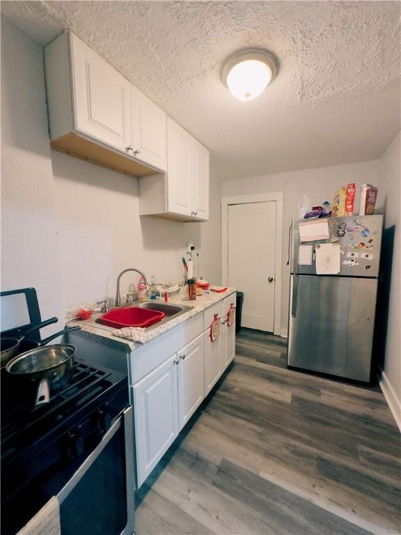 kitchen with white cabinetry, sink, stainless steel fridge, hardwood / wood-style floors, and black gas stove